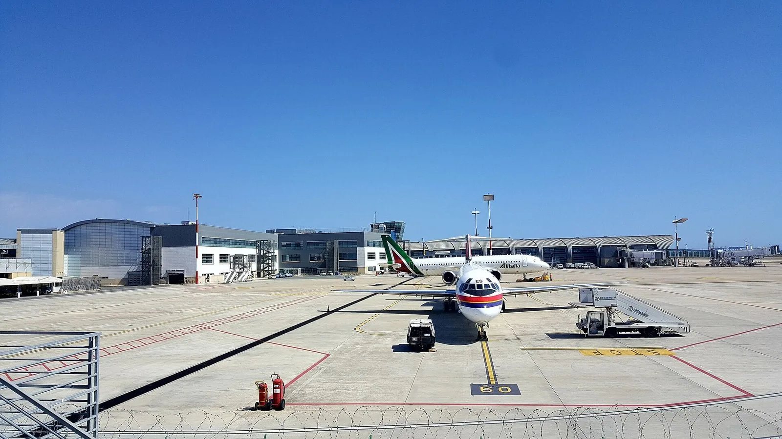 Il piazzale dell'aeroporto di Cagliari-Elmas con un aereo in sosta davanti al terminal sotto un cielo azzurro