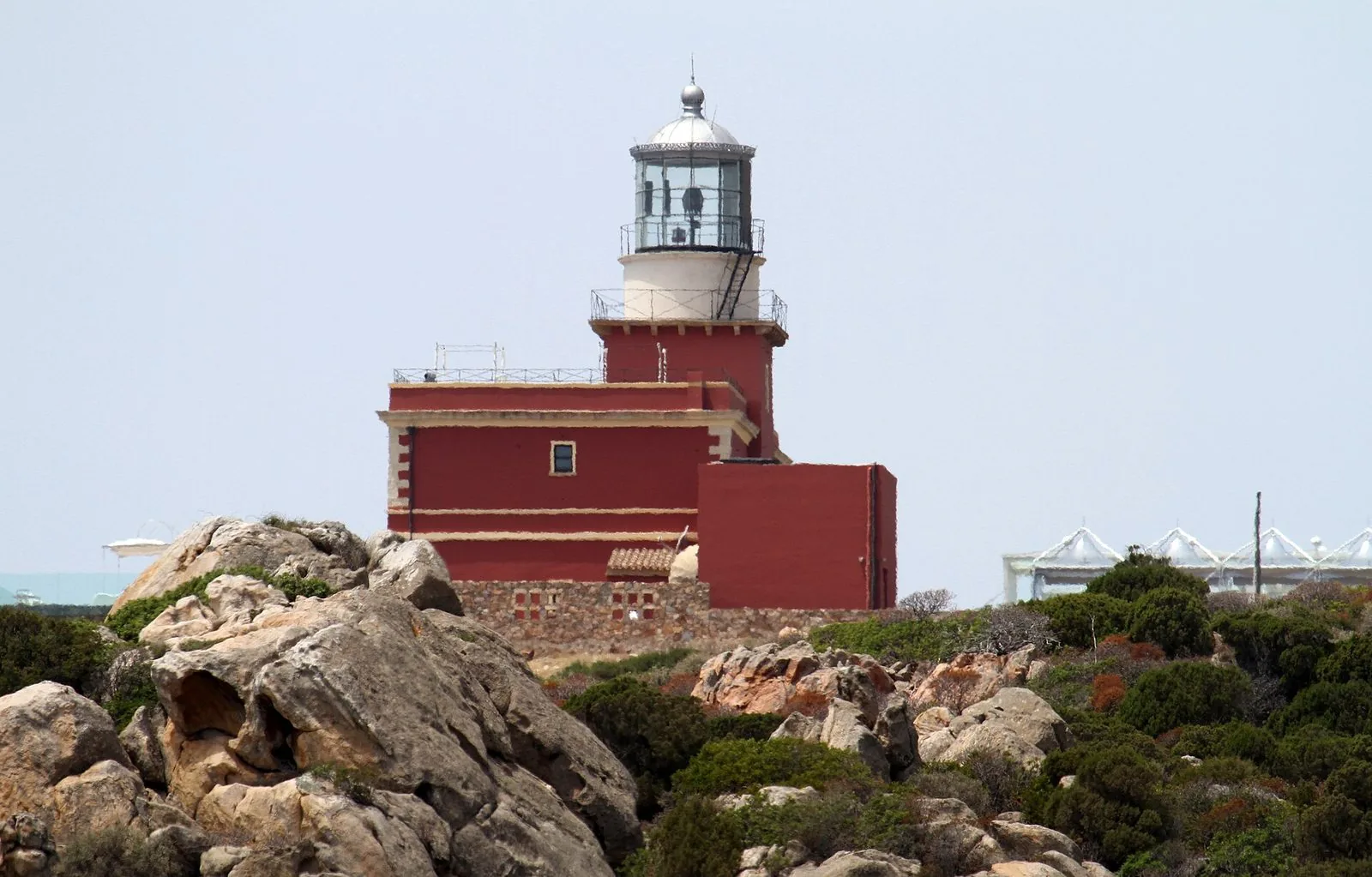Faro di Capo Spartivento: edificio rosso con la lanterna bianca, fra massi di granito e cespugli di macchia mediterranea