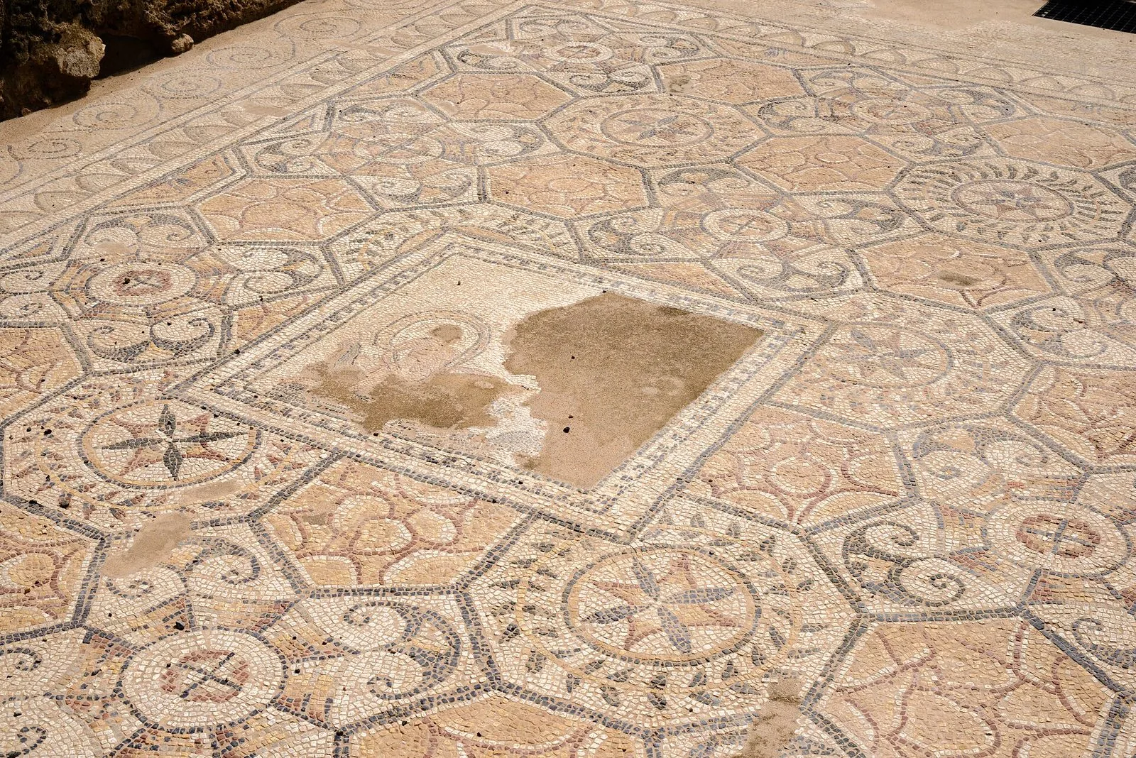 Pavimento a mosaico romano dell'area archeologica di Nora con motivi geometrici ottagonali, stelle e volute nei toni del bianco, grigio e rosa