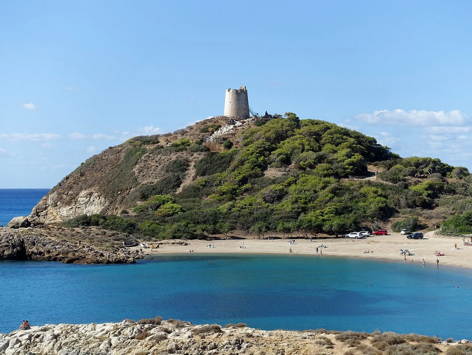 La Torre di Chia in cima a un promontorio coperto di macchia mediterranea, sopra una piccola baia turchese con spiaggia di sabbia