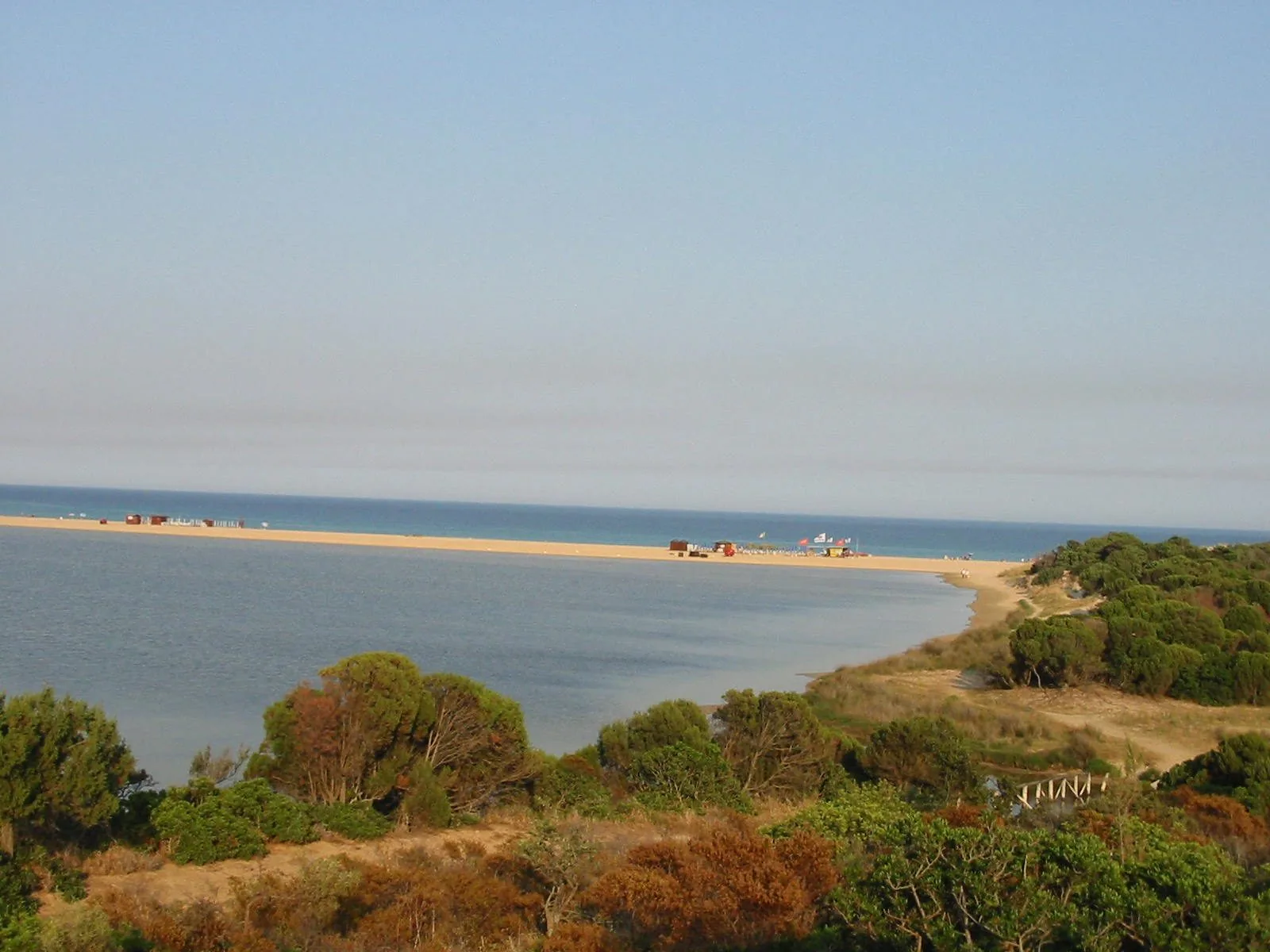 Uno stagno costiero di Chia separato dal mare da una lunga lingua di sabbia chiara, con macchia mediterranea e dune in primo piano